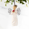 Front view of figure in cream dress with wire wings holding large red apple in hands, ornament hook on head