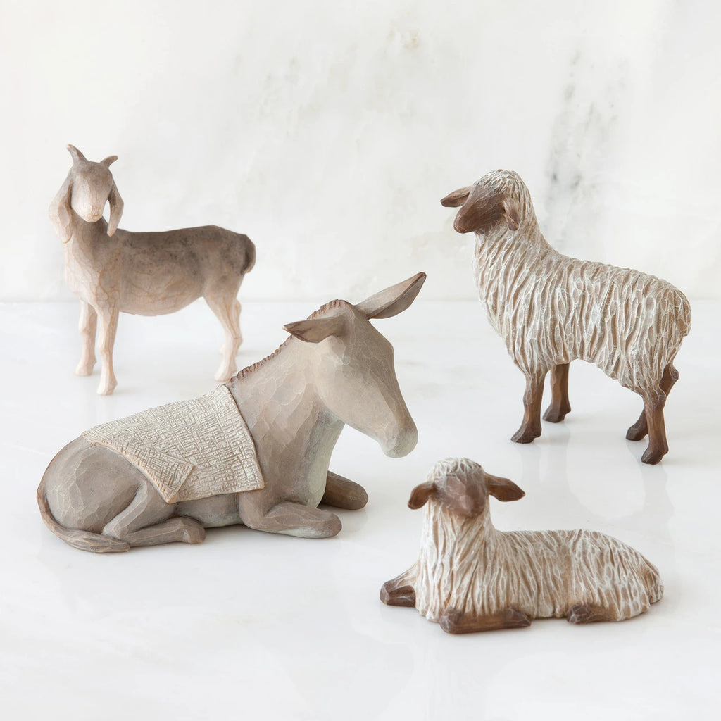 Light grey donkey figurine laying down surrounded by three sheep standing figurines