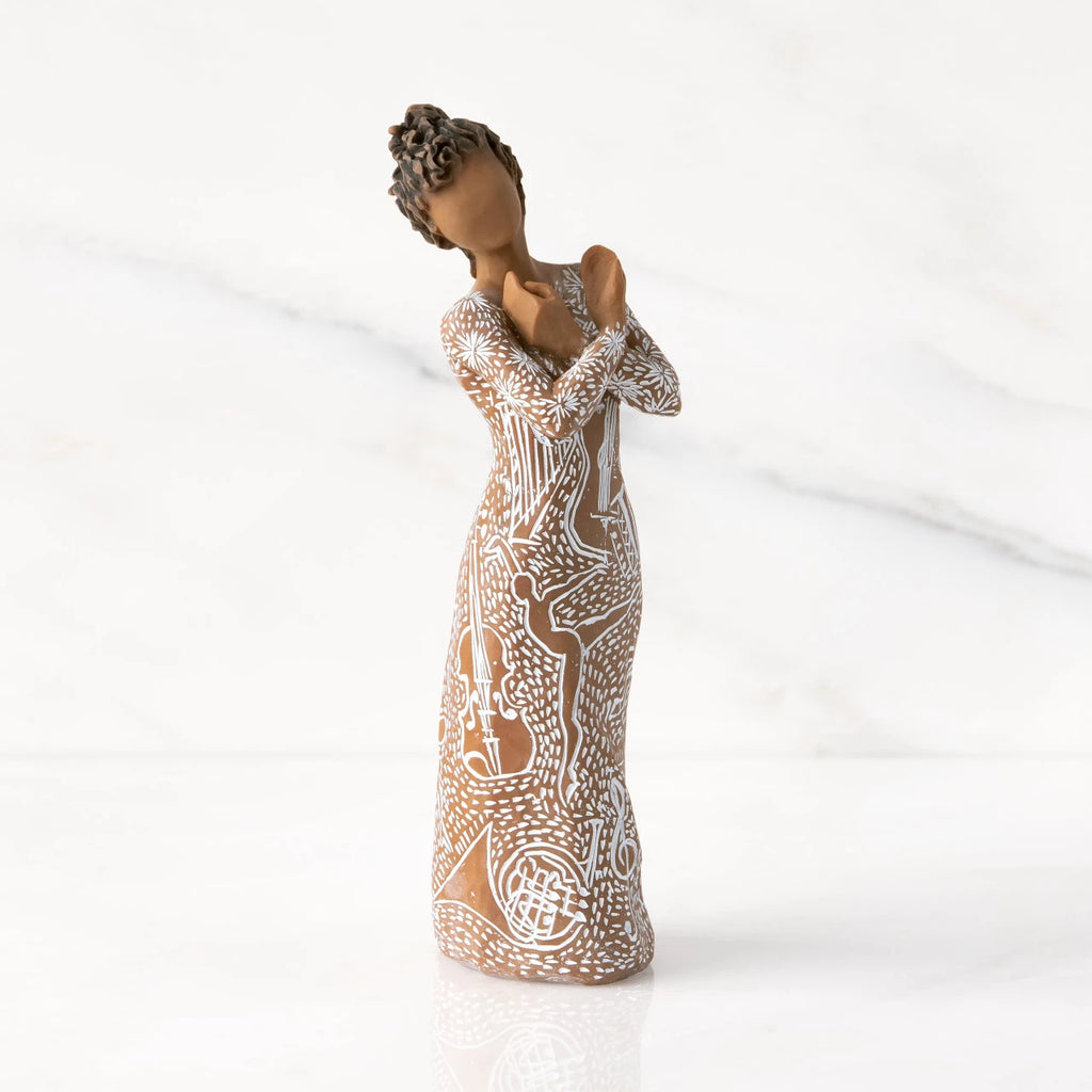 Front view: Darker-skin figure carved with contrasting pattern of white musical symbols, instruments, dancing forms