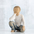 Small faceless boy figurine sitting with elbow on knee - wearing white shirt and blue jeans