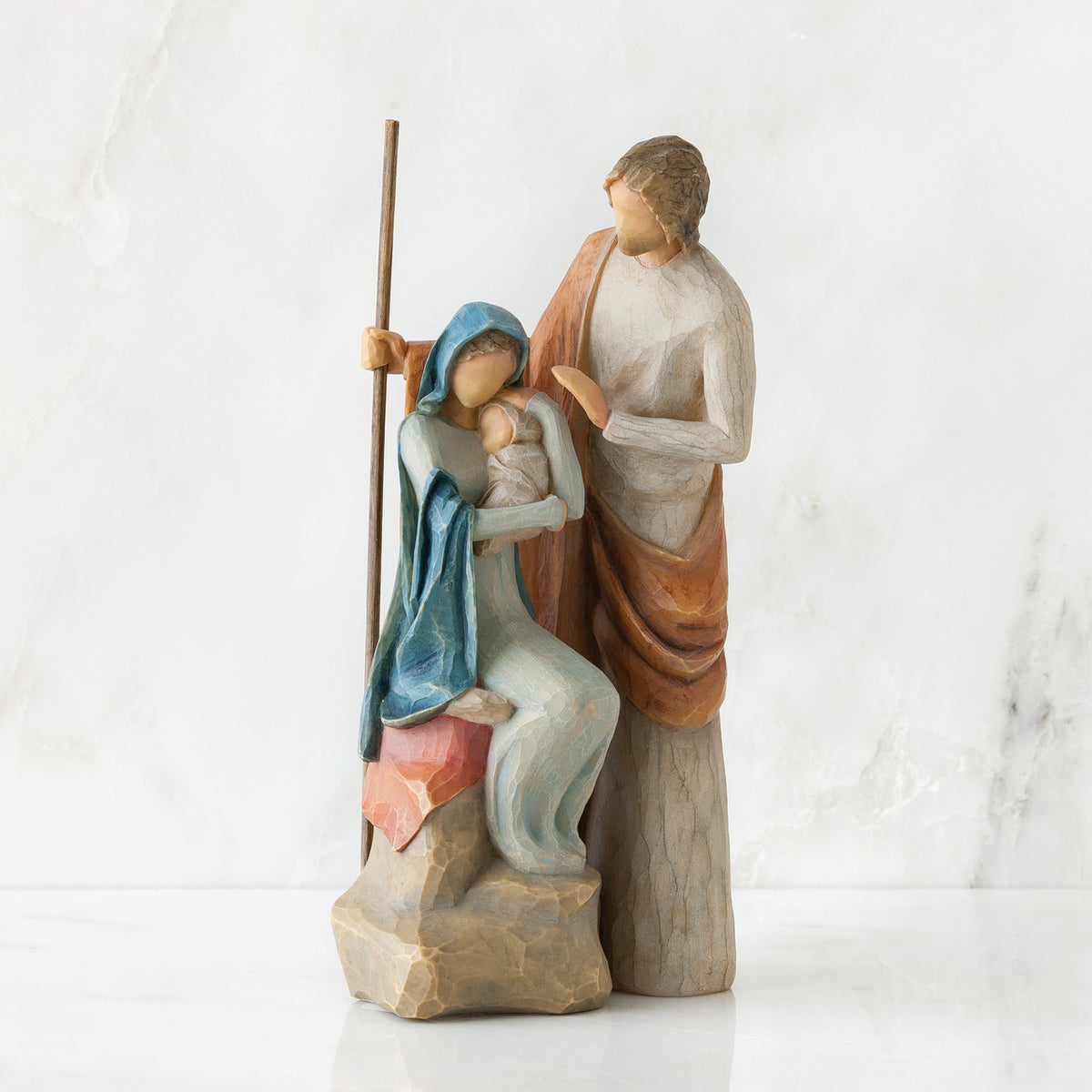 Nativity scene figurines stanging close, woman in blue is sitting on rock holding baby - man is standing above them holding a stick