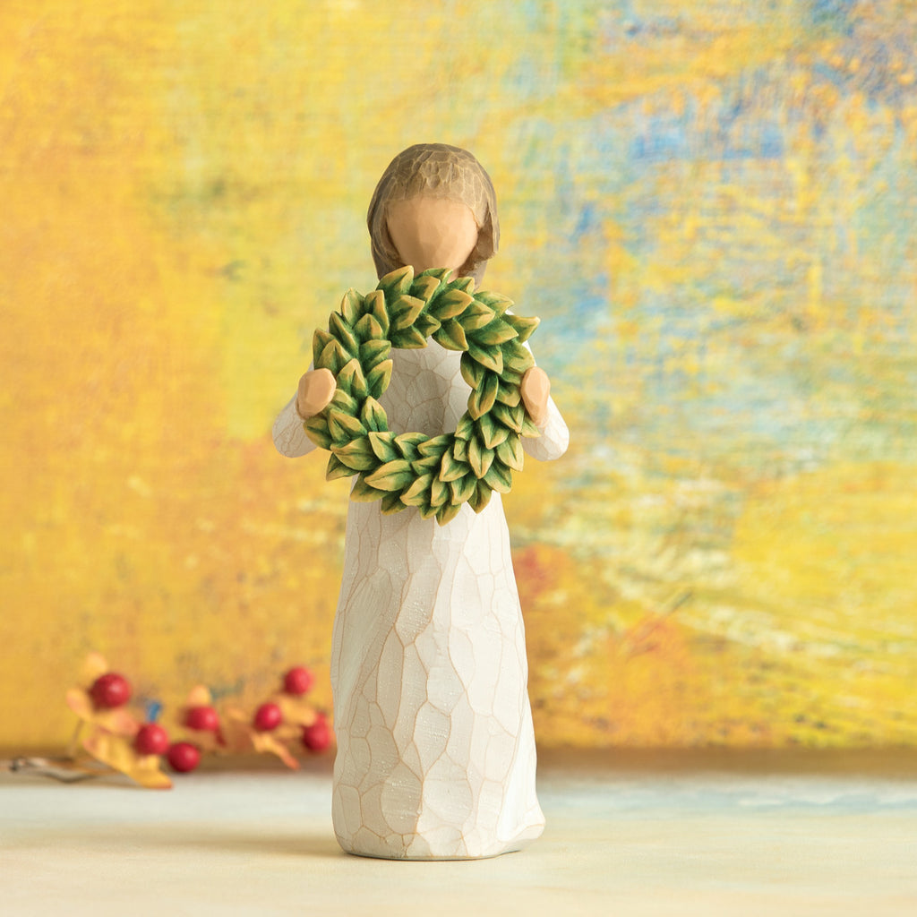 Willow Tree Magnolia, 5.5”h hand-painted standing resin figure in cream dress, holding green magnolia leaf wreath, in front of dark yellow painting