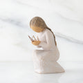 Side view of kneeling female figure in cream dress, with wire butterfly on extended hands, on marble background