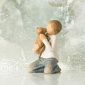 Willow Tree Kindness (boy), 3”h hand-painted resin figure of kneeling boy in neutral clothes, holding golden dog in arms, in front of gray painting