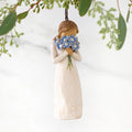 Figure in cream dress, holding large bouquet of blue forget-me-not flowers up to face. Hook and loop affixed to figure's head