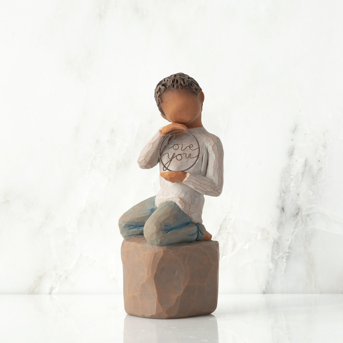 Front view: Figure of darker-skin child, kneeling on rock, holding wire circle with ‘love you’ written in wire
