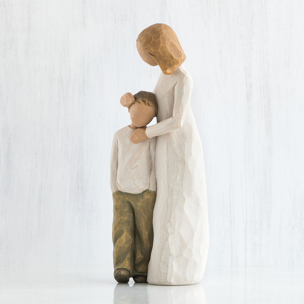 Side view of blonde mother figurine in white with hands on younger boy figurine in brown pants and white shirt