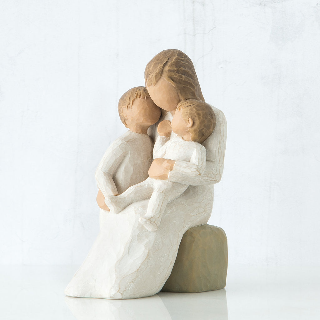Mother figurine in white dress sitting on rock holing her two baby figurines in her lap
