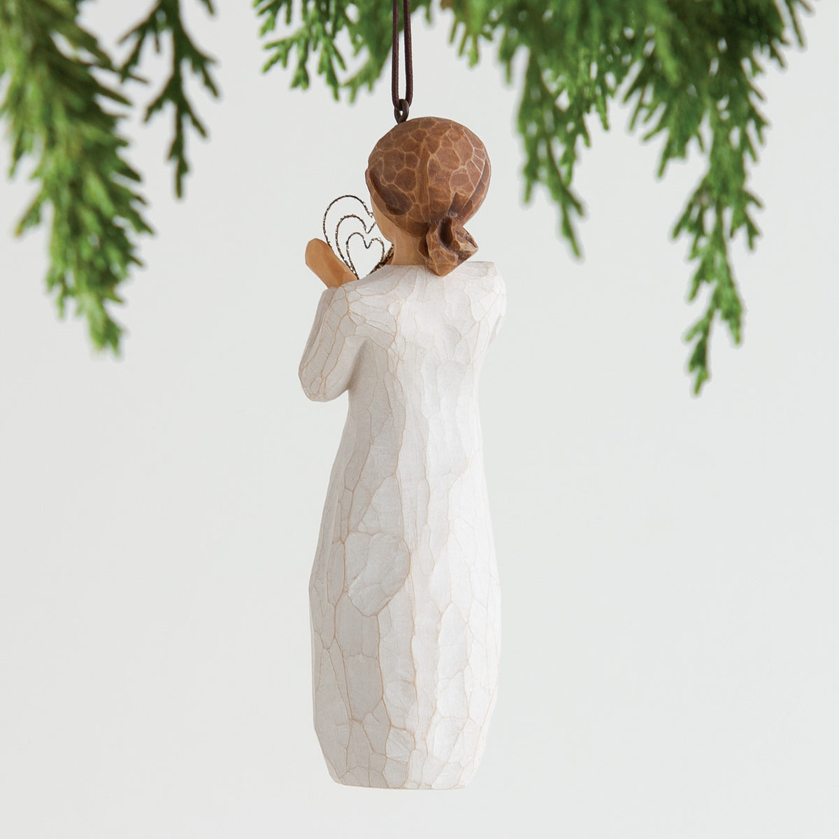 Back view of brunette girl ornament wearing white dress hung from green christmas tree