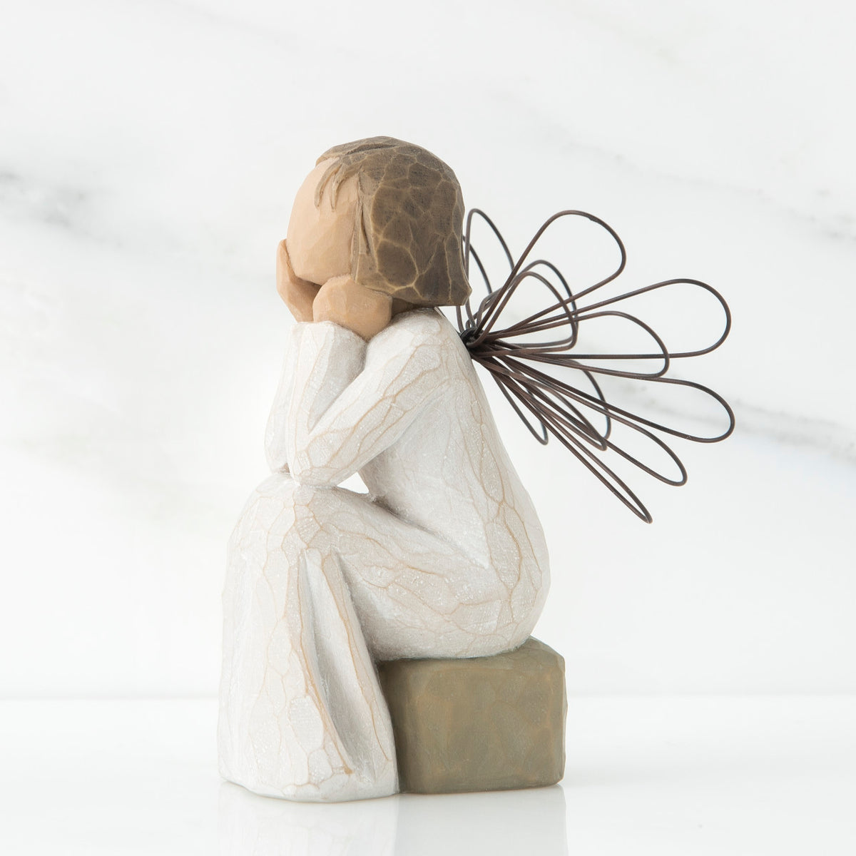 Right side view of angle with brown hair sitting on a stone with her hands cupping her cheeks