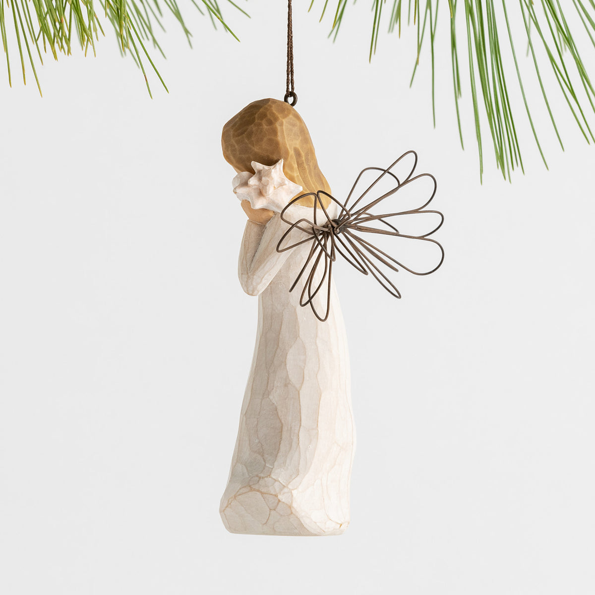 Side view female angel with wire wings in cream dress, holding pink shell up to ear, ornament loop attached to head