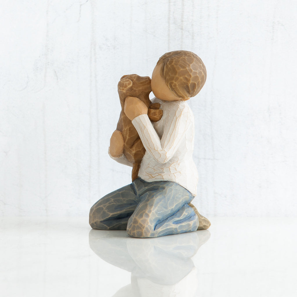 Side view of boy with light brown hair wearing white shirt and jeans and holding a light brown puppy as it licks his face.