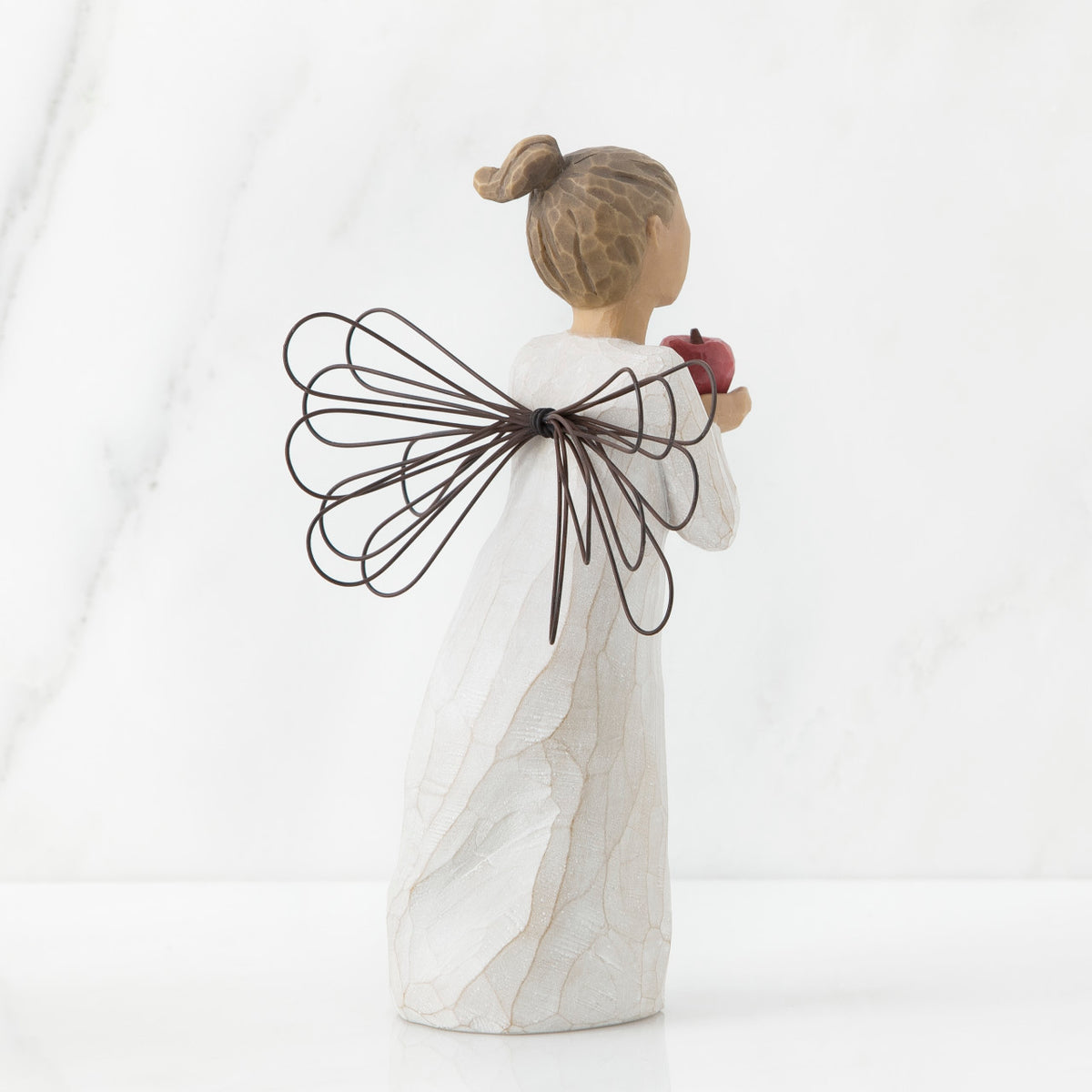 Back view of angel with brown hair in high pony tail leaning forward and holding a red apple up to her face with both hands