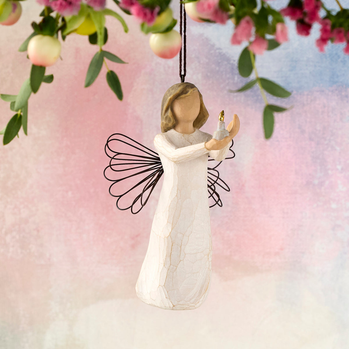 Willow Tree Angel of Hope Ornament, 4"h hand-painted resin figure in cream dress with wire wings, holding candle with gold-leaf flame in hands, brown elastic cord, hanging in front of dark yellow painting