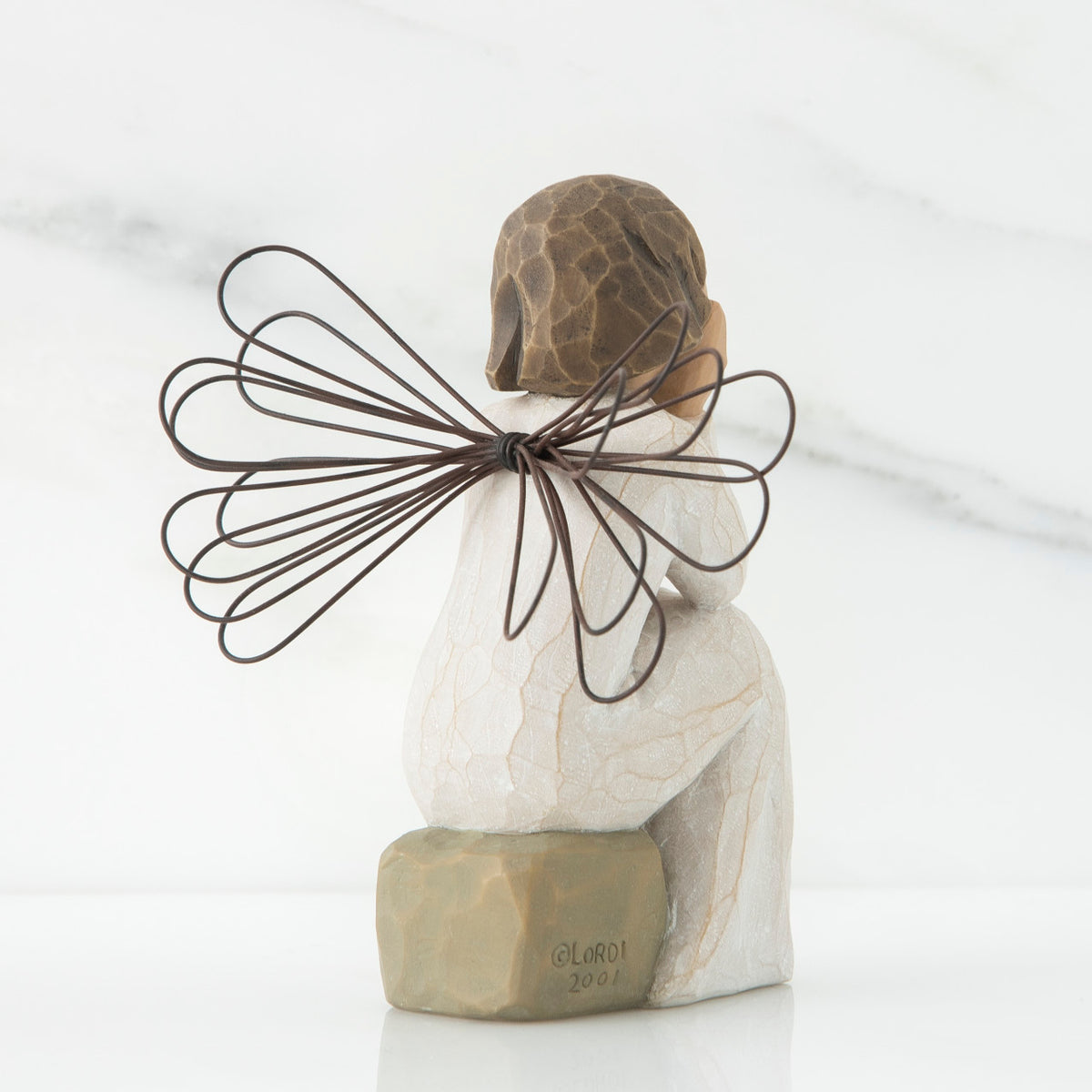 Back view of angle with brown hair sitting on a stone with her hands cupping her cheeks