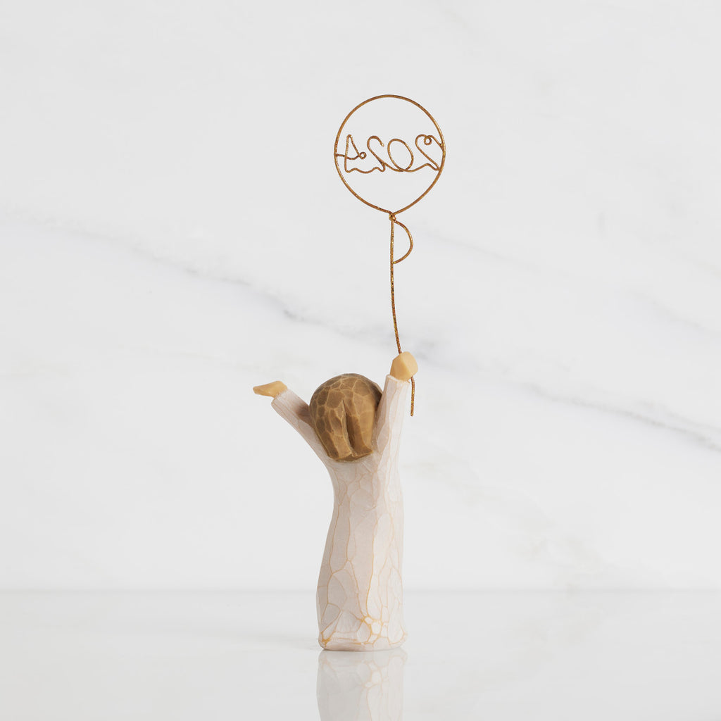 Back view: standing figure in cream dress, arms raised, holding gold wire balloon with 2024 written in gold wire inside
