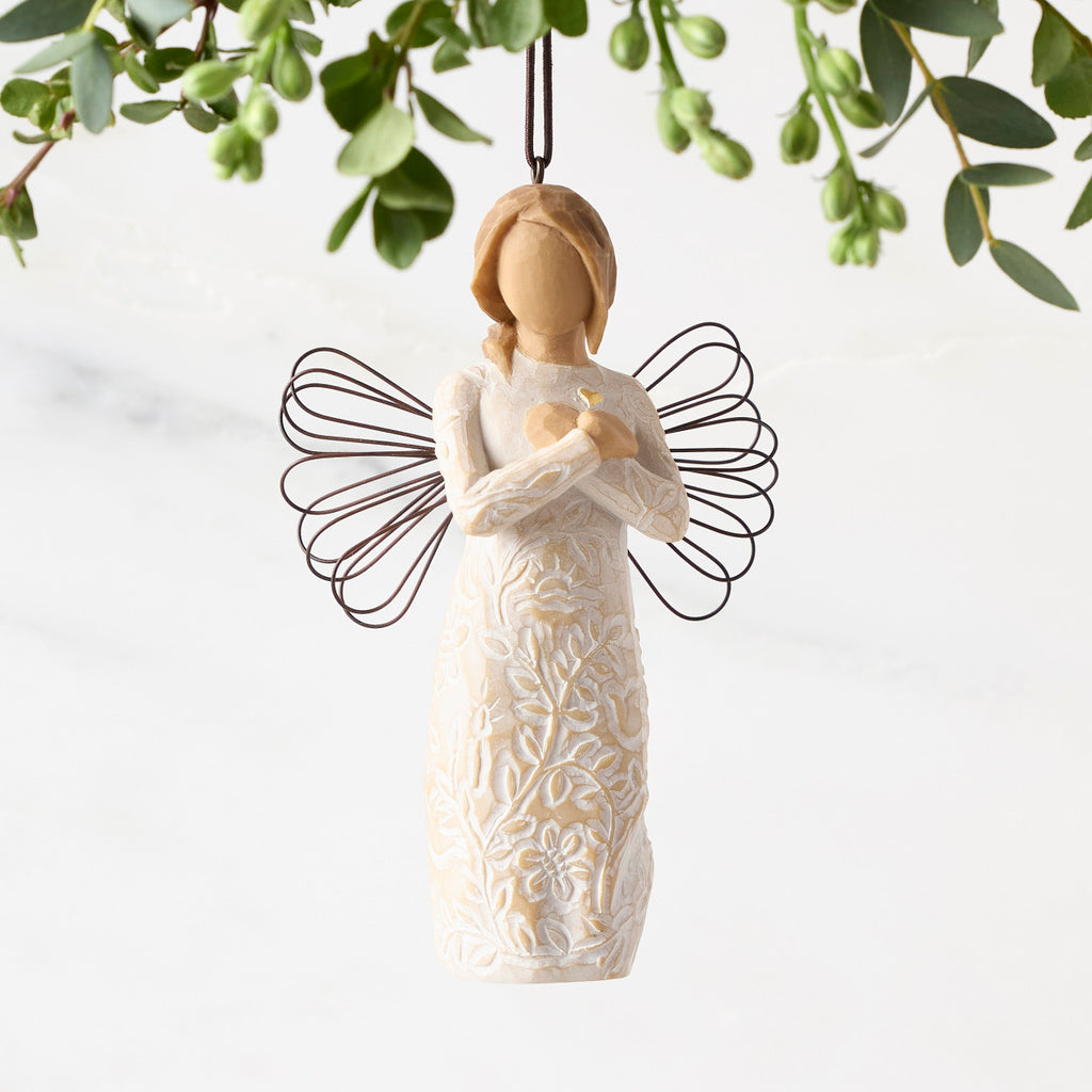 Front view of figure in cream dress carved with symbols of nature with wire wings, hands folded at chest around gold heart, ornament hook on head