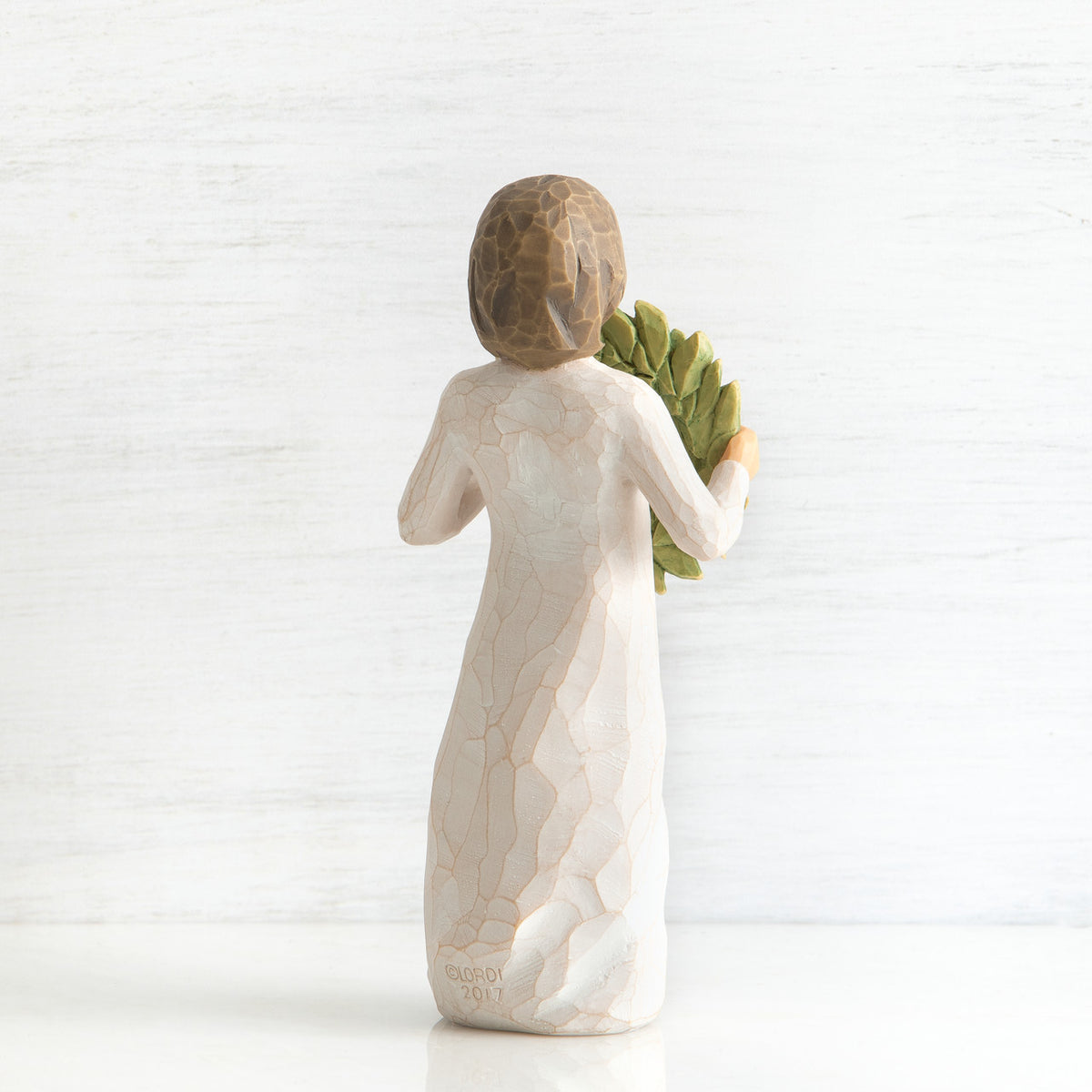 Back view of young girl with bangs and short brown hair holding up a green, leafy wreath