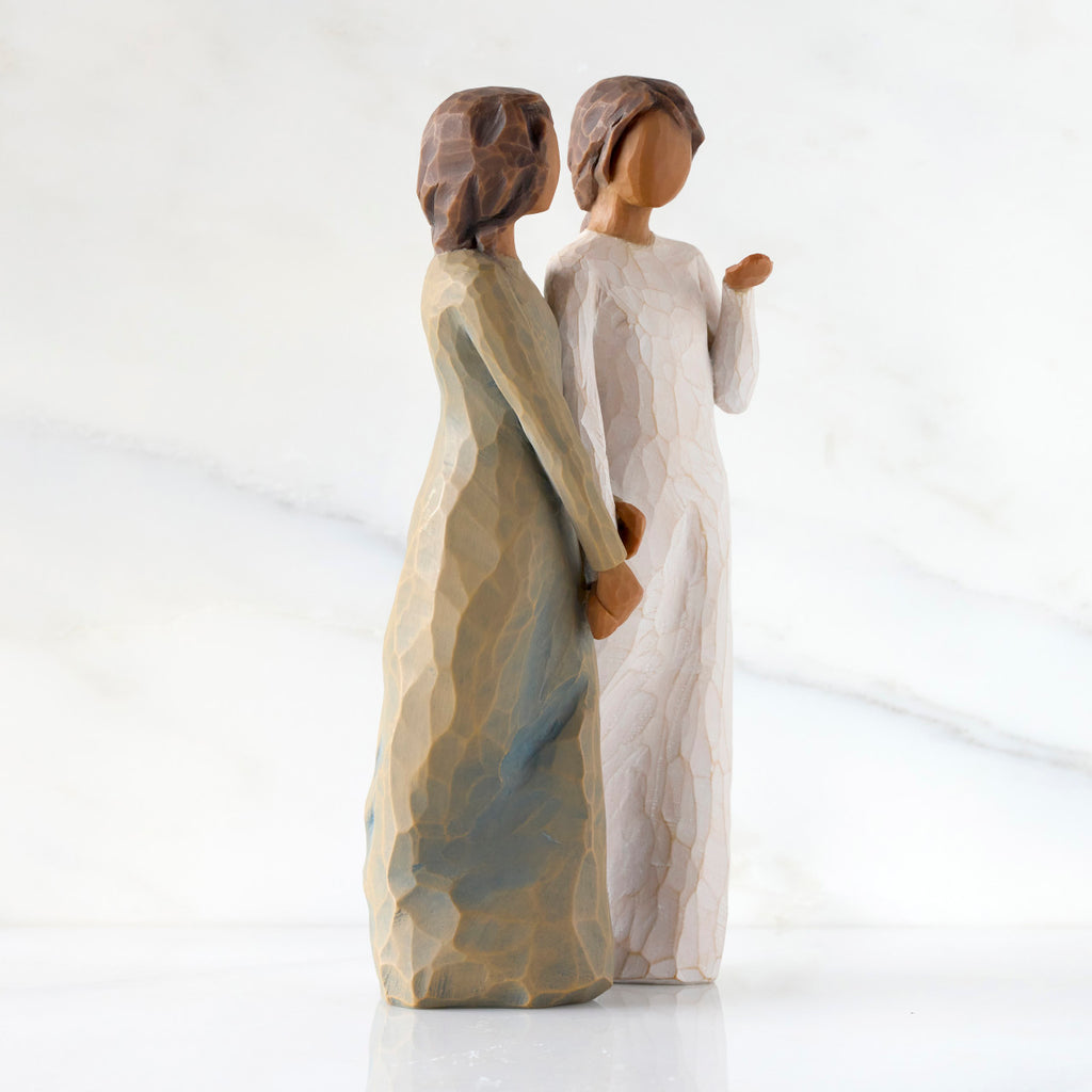Right-facing view: Figure of two women with darker skin tones in different colored dresses, standing arm in arm