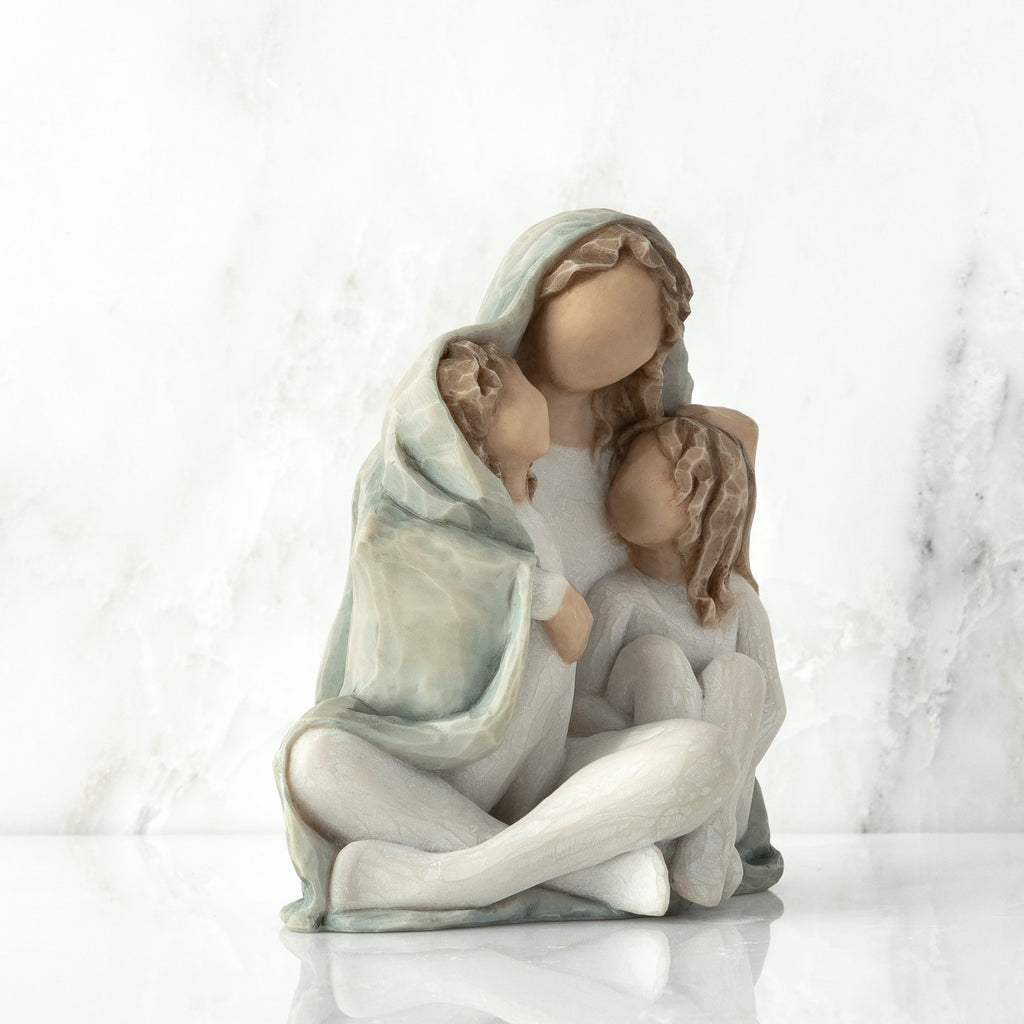 Right view: seated figure with arms around two younger figures, all wrapped in a blue-gray blanket