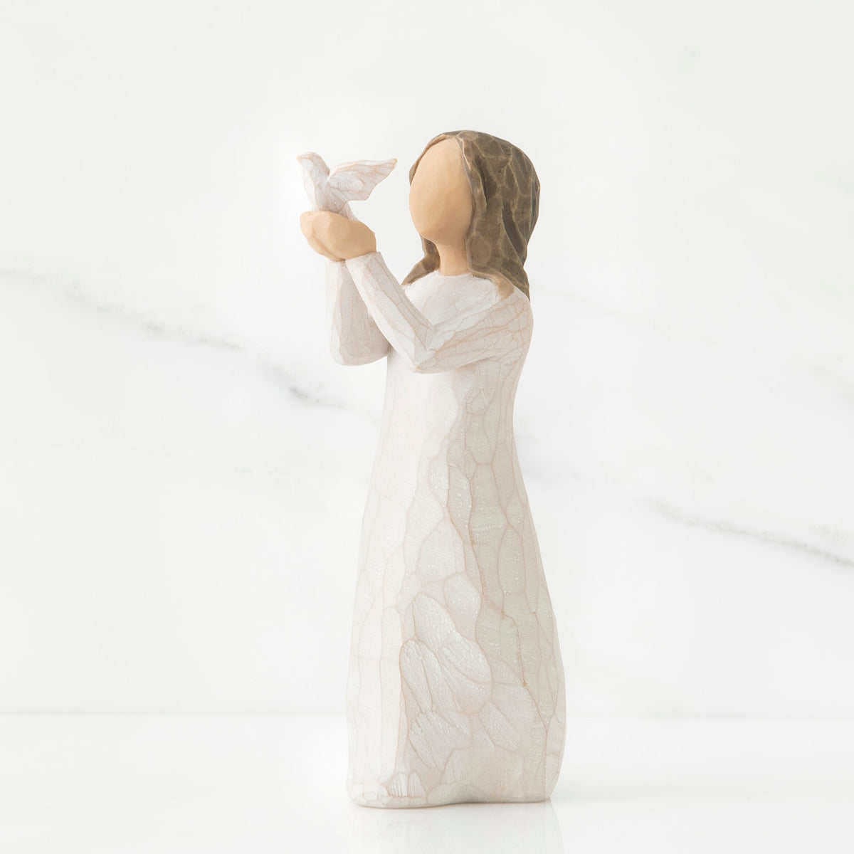 Faceless woman figurine in white dress holding up white bird in her arms