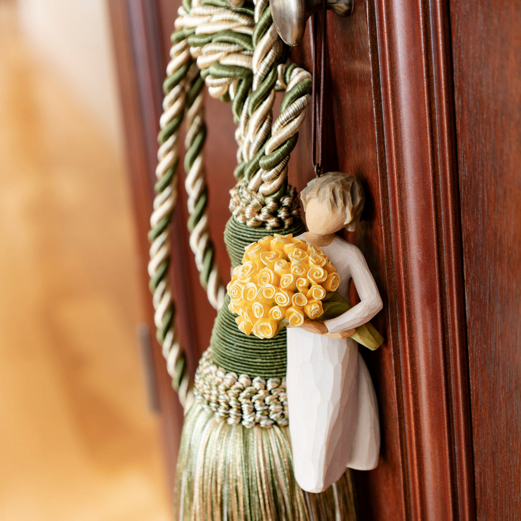 Willow Tree Good Cheer! Ornament, 4.5”h hand-painted resin figure in cream dress, holding bouquet of yellow roses, brown elastic cord, hanging on doorknob