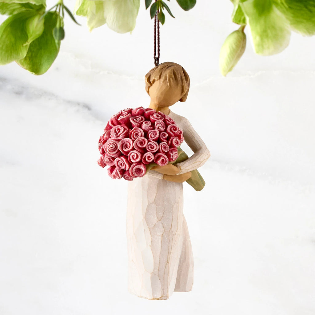 Front view of female figure with short brown hair holding large bouquet of pink roses, ornament loop affixed to top of head