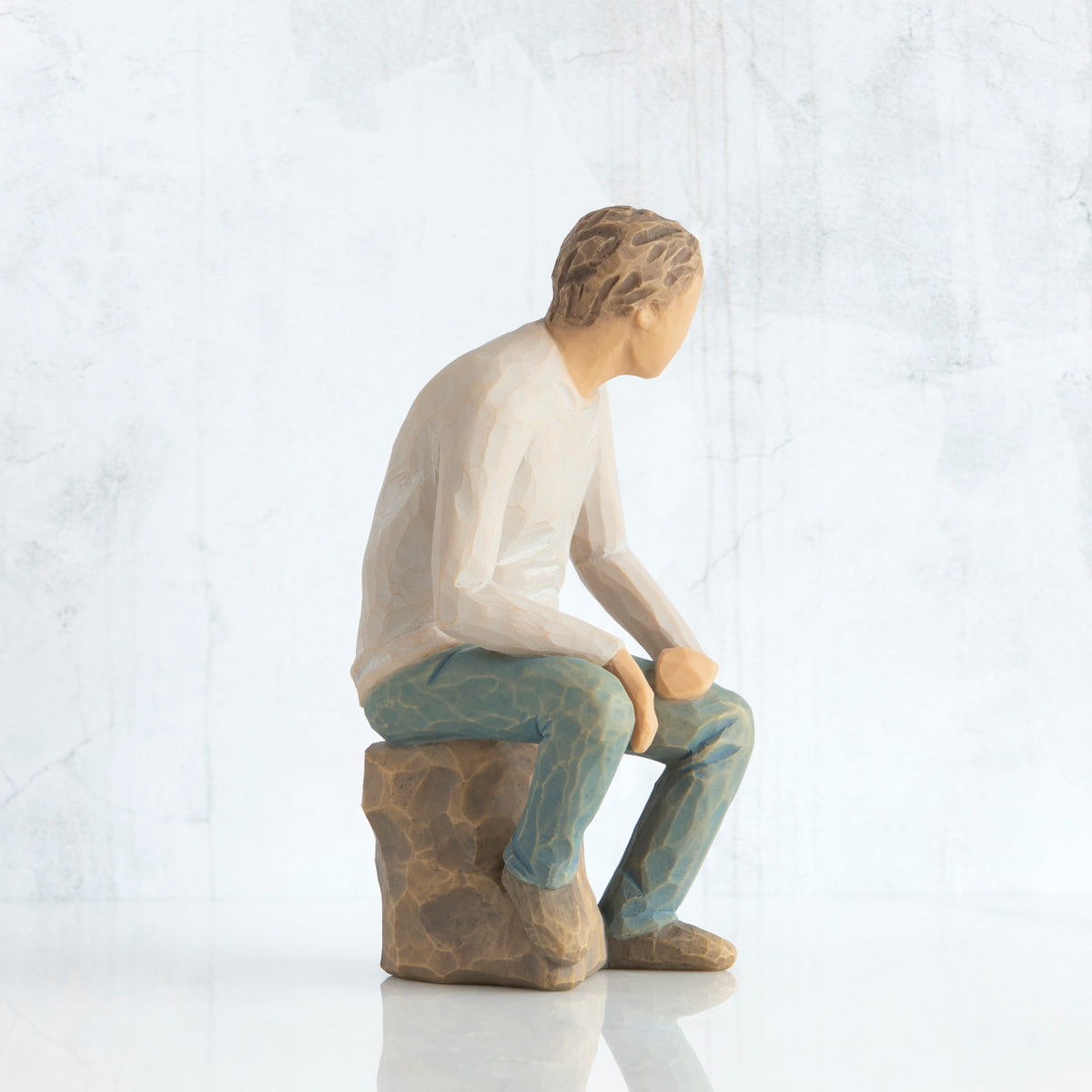 Right-facing view, adult male figure in light gray shirt and blue jeans, seated on gray rock