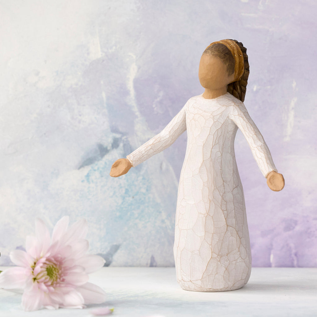 Willow Tree Blessings, 5.5”h hand-painted resin figure in cream dress with darker skin and hair, wearing glitter headband, arms stretched out to sides, in front of light purple painting