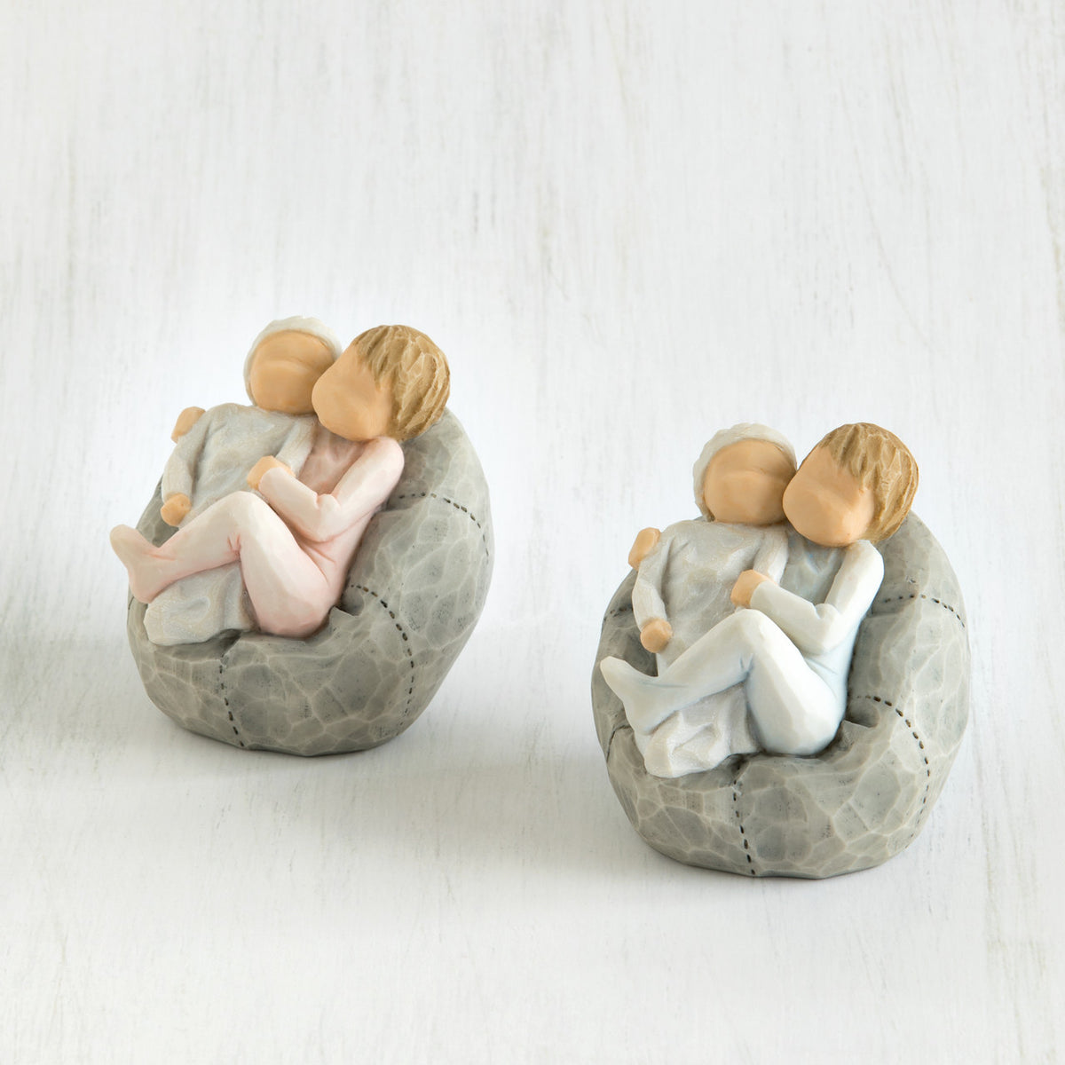 Set of two baby figurines being held by their siblings on grey beanbags