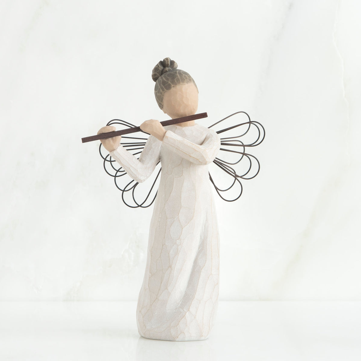 Faceless angel figurine wearing white dress and black wire wings playing black flute