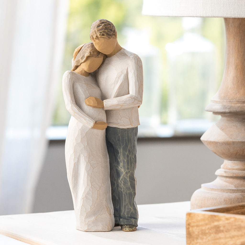 Willow Tree Home, 8.5”h hand-painted standing figure of man and pregnant woman embracing, both in neutral clothes, on table near window