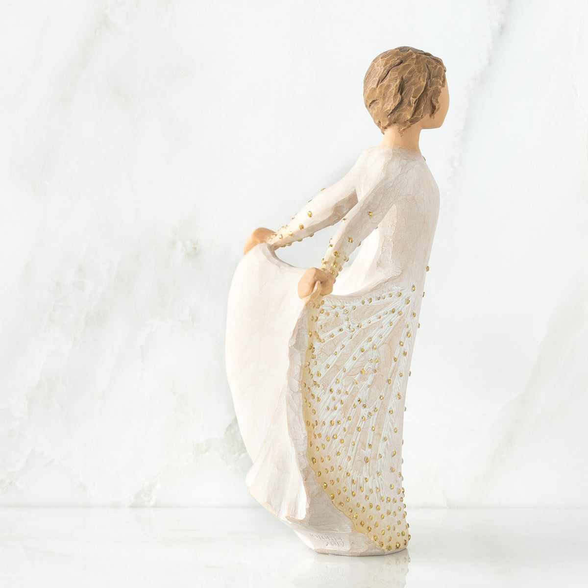 Brunette girl figurine holding up white and gold polka dot dress facing the side
