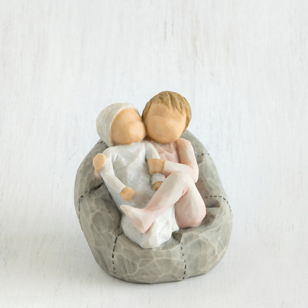 Two small baby figurines hugging another laying on grey beanbag