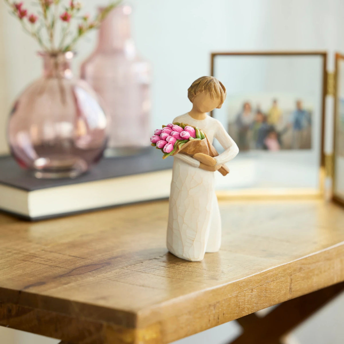 Willow Tree Bright Hope, 4”h hand-painted standing figure in cream dress, holding bouquet of bright pink tulips, on wood desk with photos