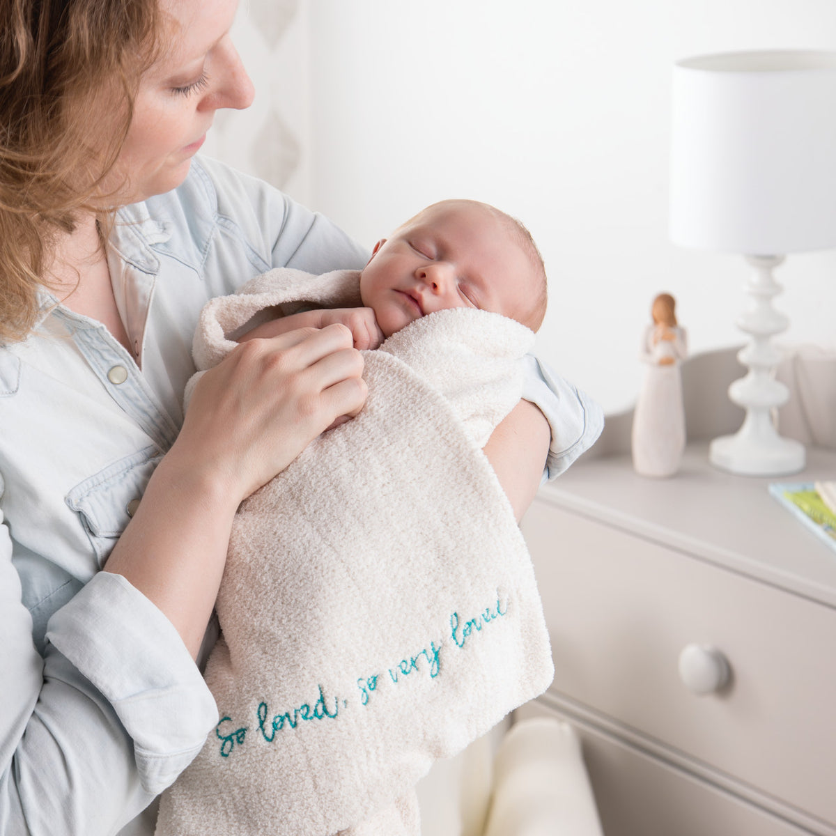 Side view of mother holding swaddled baby in light pink