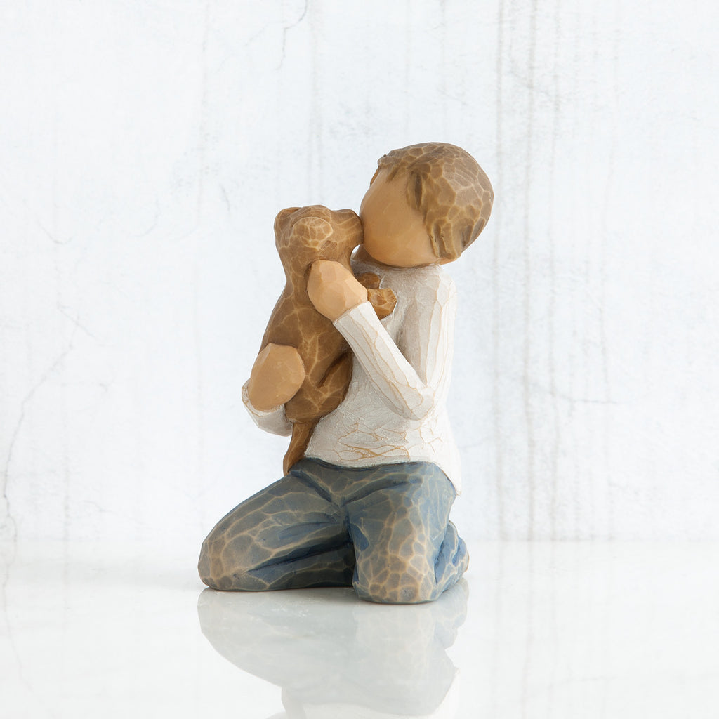 Front view of boy with iight brown hair wearing white shirt and jeans and holding a light brown puppy as it licks his face.